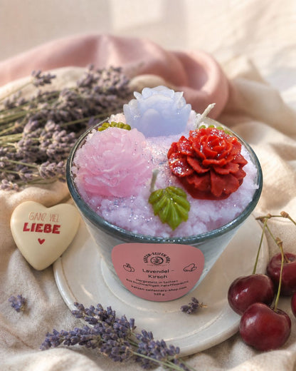 Lavendel-Kirsch Duftkerze auf heller Steinplatte mit rosa Tuch, Lavendel und Kirschen