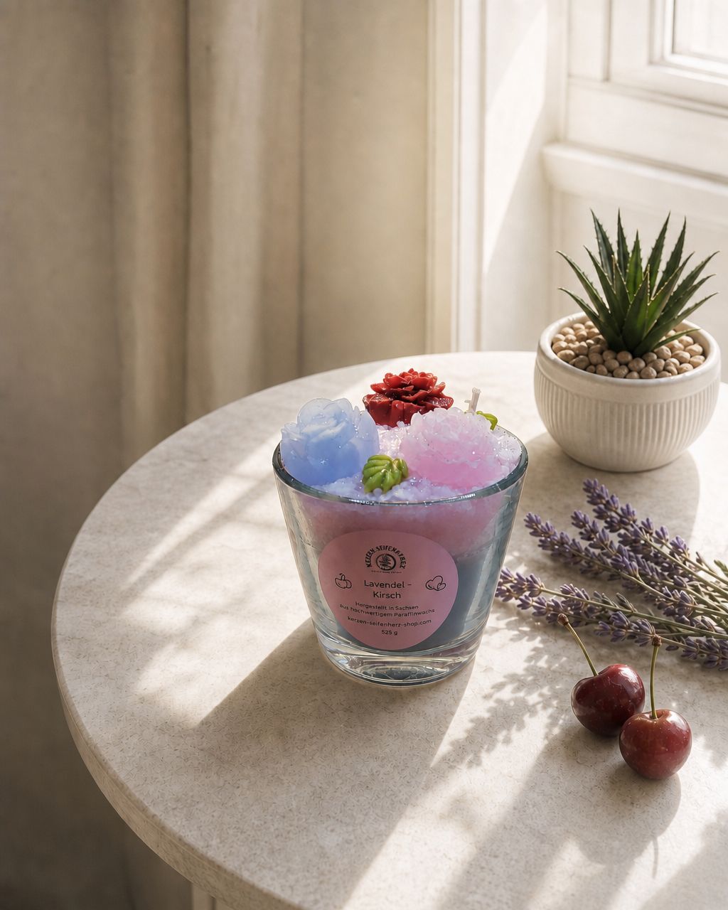 Lavendel-Kirsch Duftkerze auf rundem Tisch am Fenster mit Pflanze, Lavendel und Kirschen