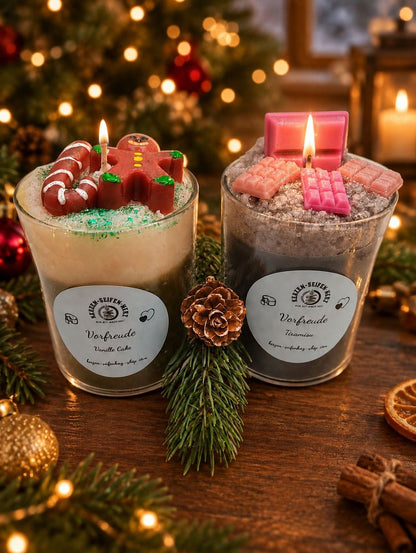 Weihnachtskerzen-Set Vanillecake und Tiramisu gemeinsam mit Tannengrün vor warmem Weihnachtslichter-Hintergrund